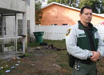CPL. ROBERT CAPIZZI STANDS OUTSIDE A FORECLOSED PROPERTY DETERMINED TO HAVE MORE THAN $90,000 IN CODE VIOLATIONS DURING A DISTRESSED PROPERTY SWEEP IN GOLDEN GATE. CPL. CAPIZZI’S COMMUNITY CLEANUP EFFORTS HAVE EARNED HIM THE 2016 NATIONAL LAW ENFORCEMENT OFFICER OF THE YEAR AWARD FROM KEEP AMERICA BEAUTIFUL.